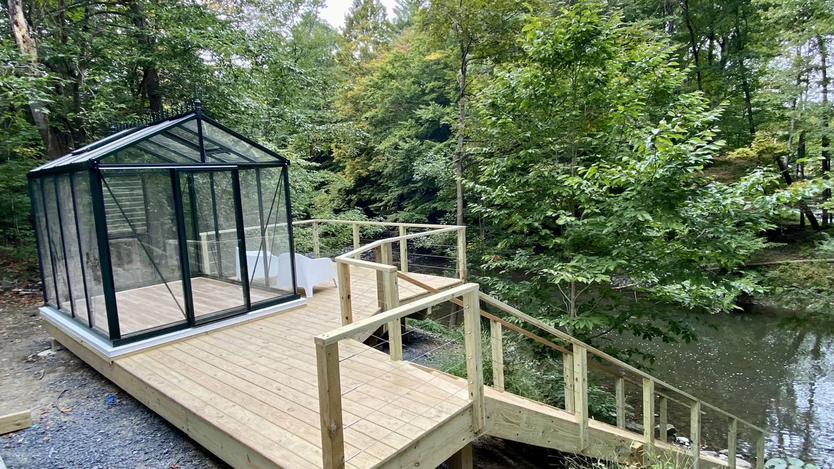 New wooden deck, stairs and railings beside a creek, with a small greenhouse on the deck